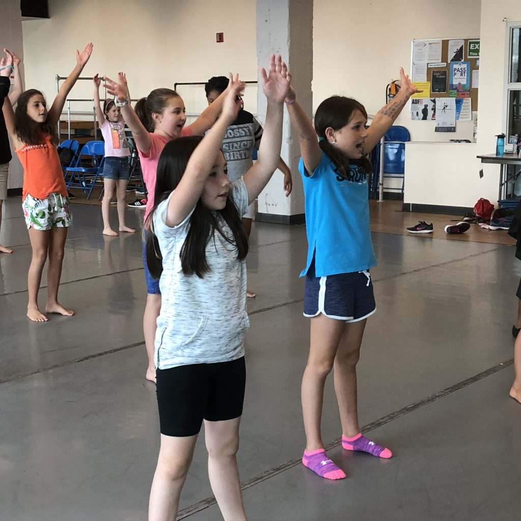 Kids raise their arms in a dance studio