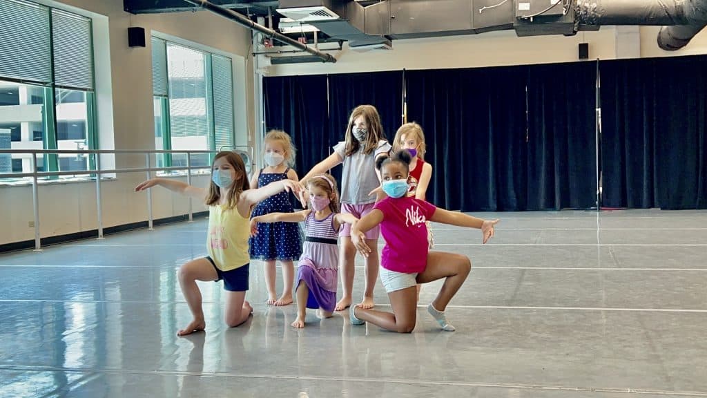 A mixed group of young dance students kneeling in a pose after a performance in the studio.