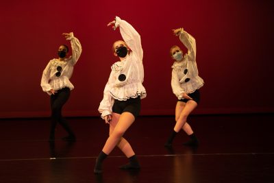 Three Teen Performance Company dancers performing on stage in clown-themed costumes.