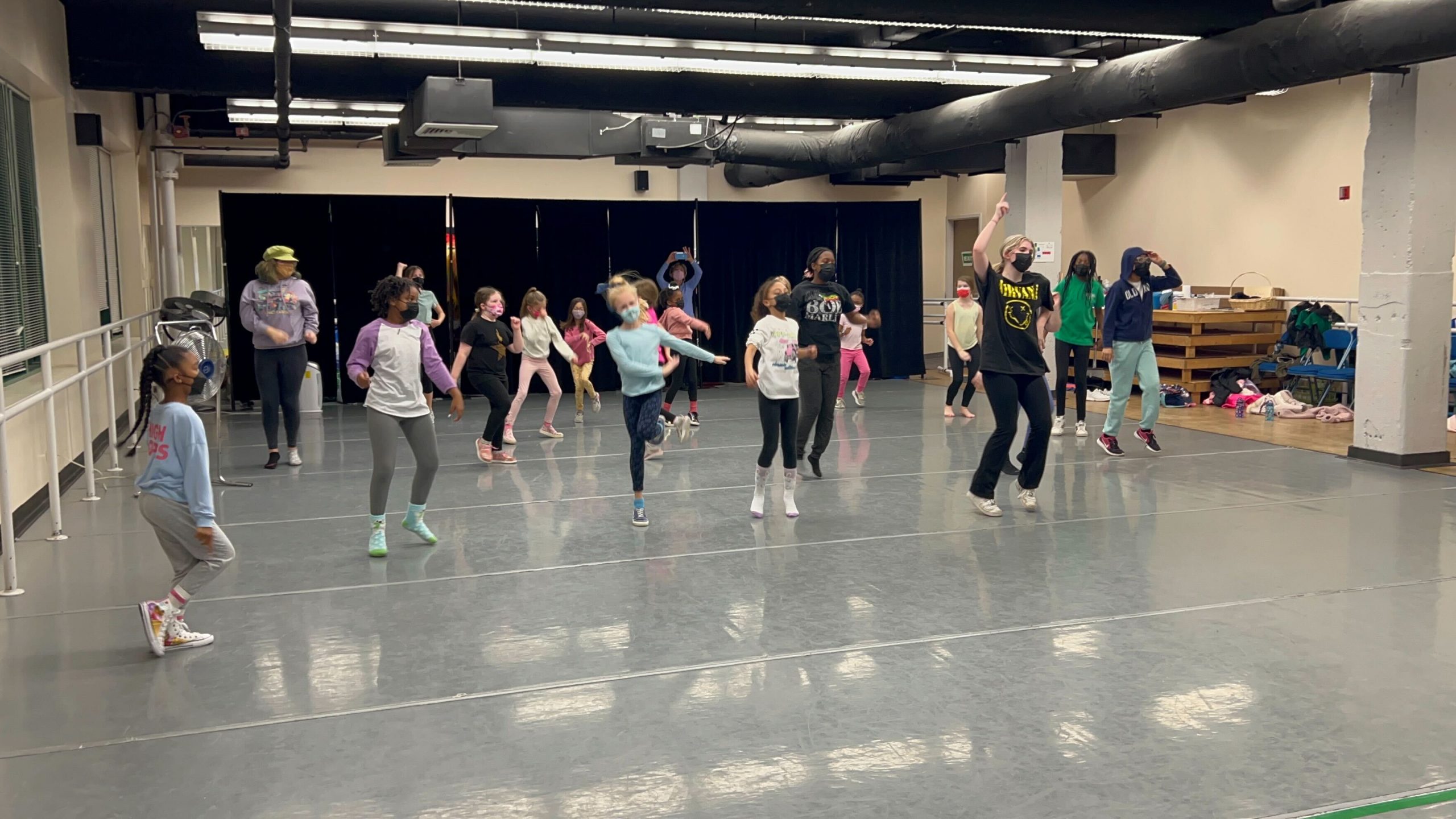 A large group of kids rehearsing a dance in a dance studio.