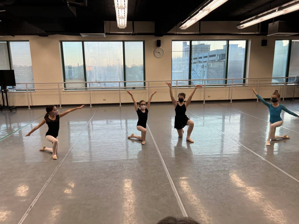Dance studio with four youth dancers kneeling as if at the end of a performance.