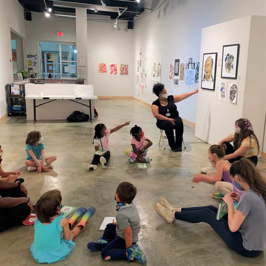 Children sitting in a circle looking at art.