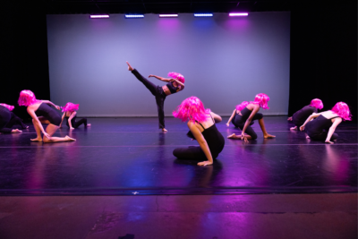 Several teen dancers in tight black pants and tops and bright pink wigs perform during Dance Project's Spring showcase.