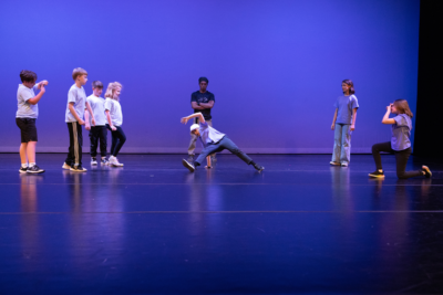 A youth breakdancing class performs during Dance Project's Spring showcase, with one dancer breaking in the middle and the other dancers looking on.