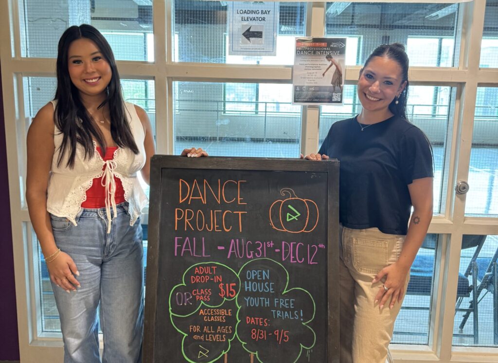 Two college-aged women, interns at Dance Project, pose outside the dance studio.