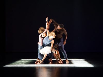 A mixed group of professional adult dancers performing Helen Simoneau's Flight Distance I are tightly intertwined together on stage.
