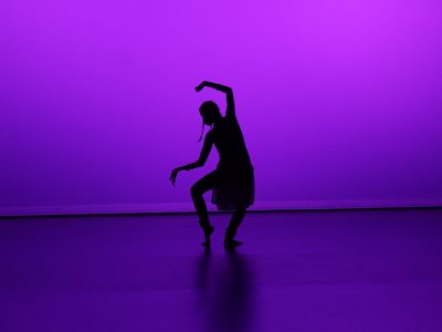 Indian dance choreographer Aparna Keshaviah is silhouetted against a purple stage backdrop.