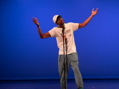 A man on a stage gestures with his arms while performing poetry.