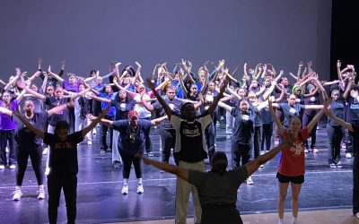 A large group of high school dance students stand with their arms raised during a master class with Christa Oliver in the Van Dyke Performance Space.